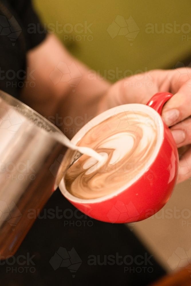 barista pouring the milk into a flat white coffee - Australian Stock Image