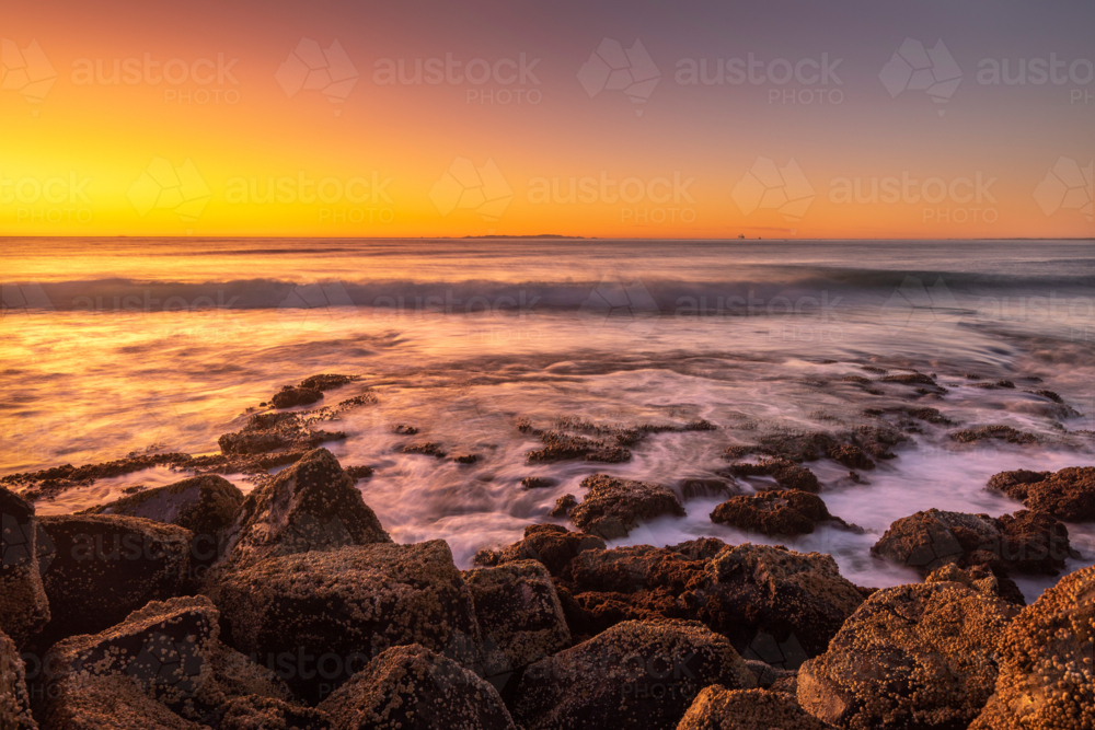 Barnacle covered rocks at sunset with waves crashing - Australian Stock Image