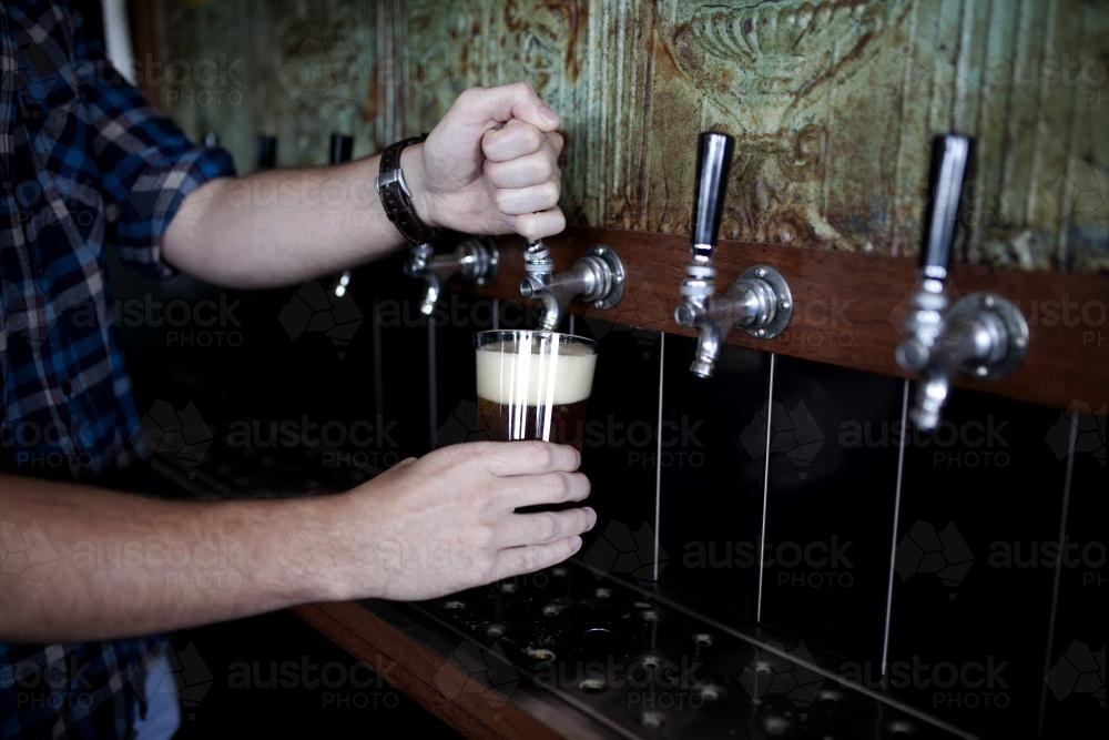 Bartender pouring drink on tap at local craft beer bar - Australian Stock Image