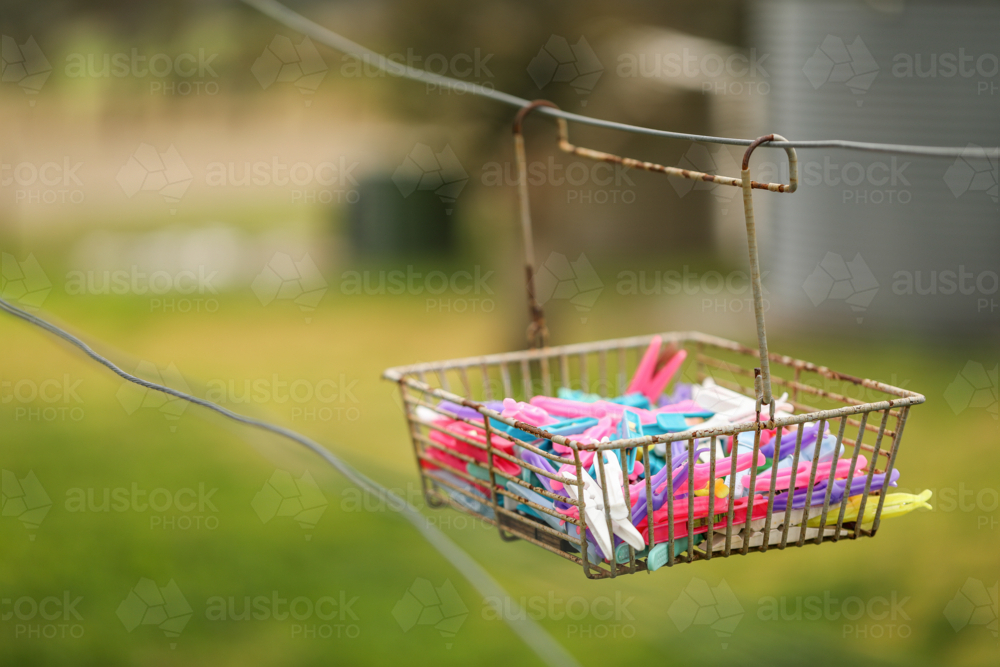 Basket of brightly coloured clothes pegs hanging on washing line - Australian Stock Image