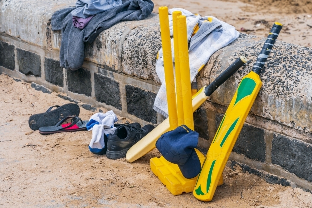 Beach cricket equipment and clothing sitting on a stone wall at the beach. - Australian Stock Image