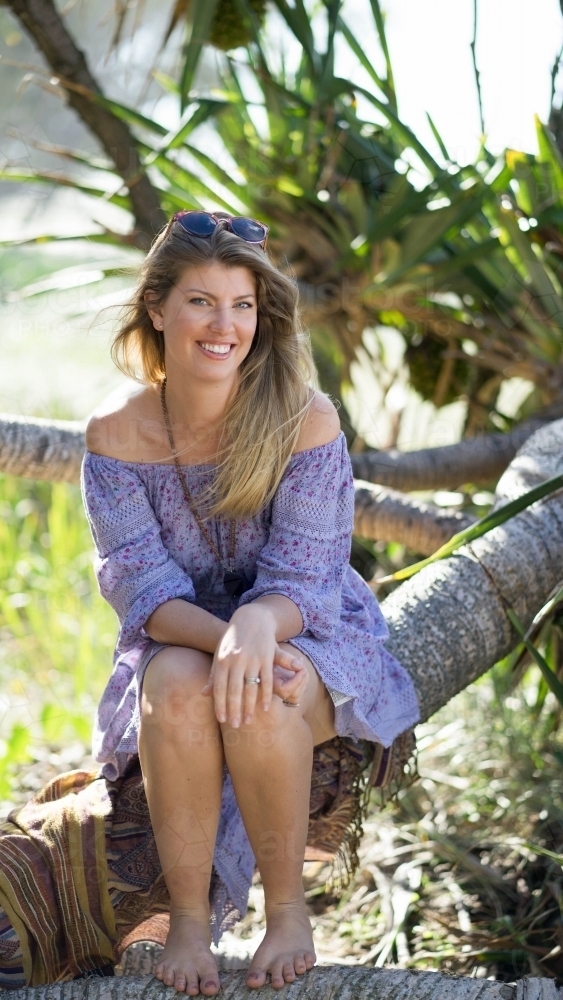 Beach girl sitting on tree branch on beach - Australian Stock Image