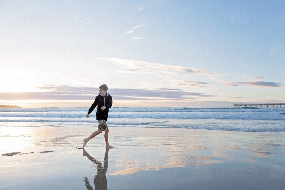 Beach reflections with boy running on wet sand - Australian Stock Image