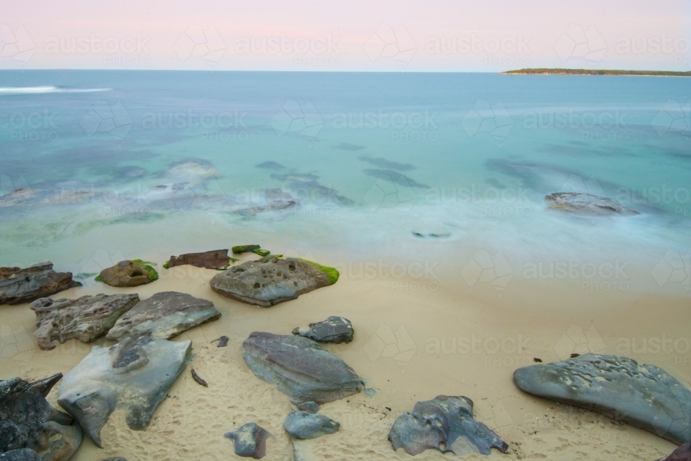 Beach, rocks and ocean at sunset with blurred motion of waves - Australian Stock Image