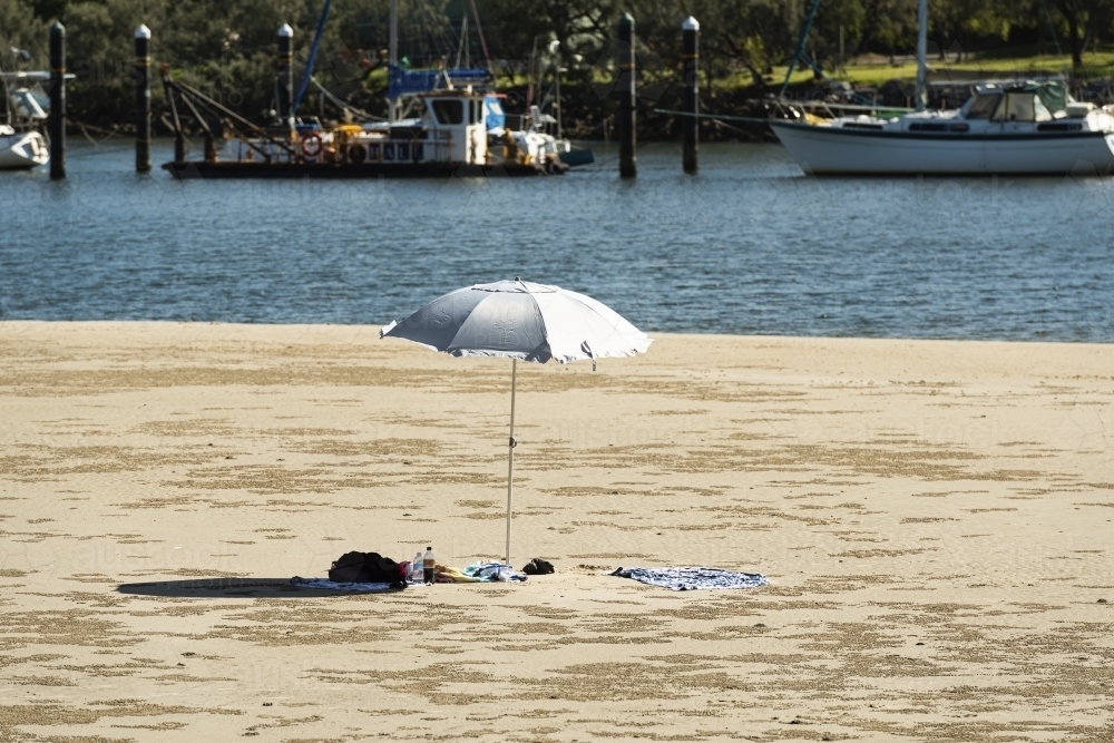 Beach umbrella in beach each scene at rivers edge with boats moored in water - Australian Stock Image