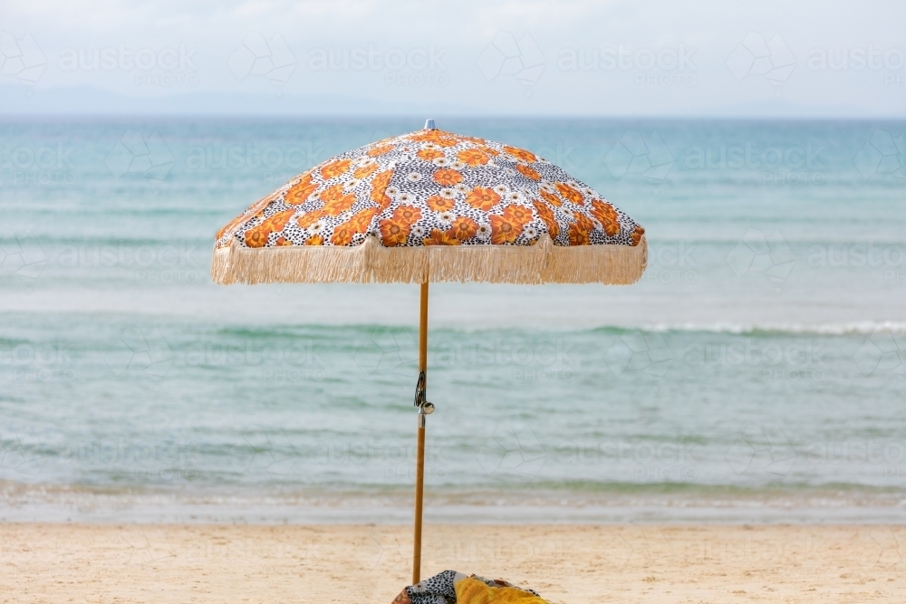 Beach umbrella on sand in front of ocean - Australian Stock Image