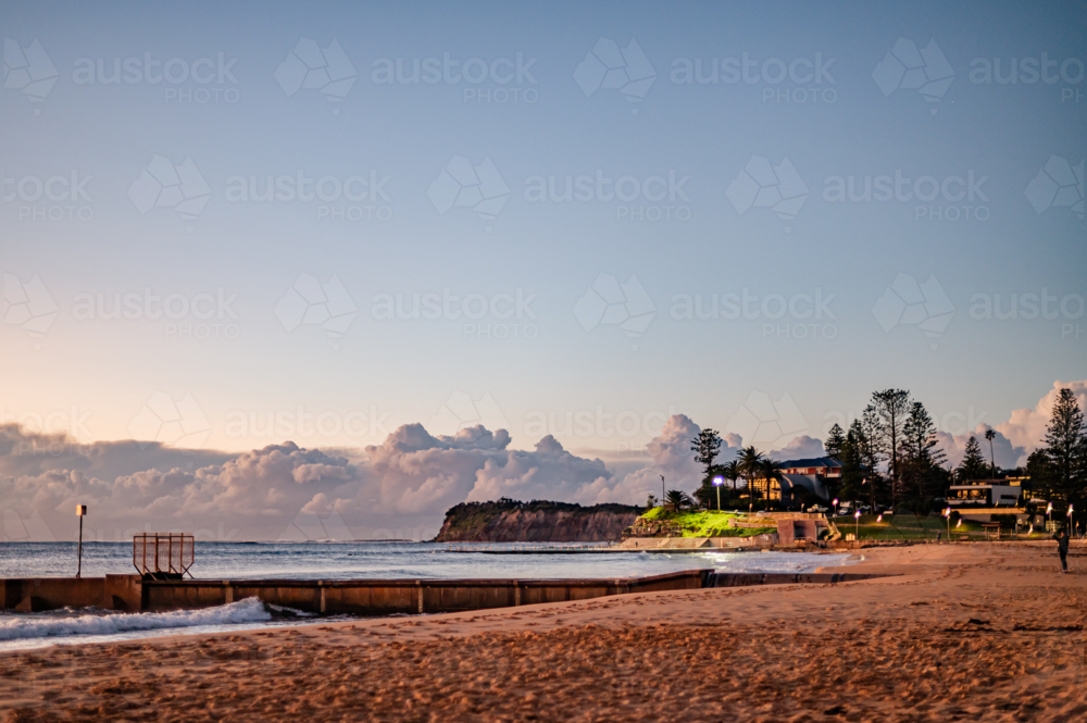 Beach with Seawall and Distant Cliffs at Sunrise - Australian Stock Image