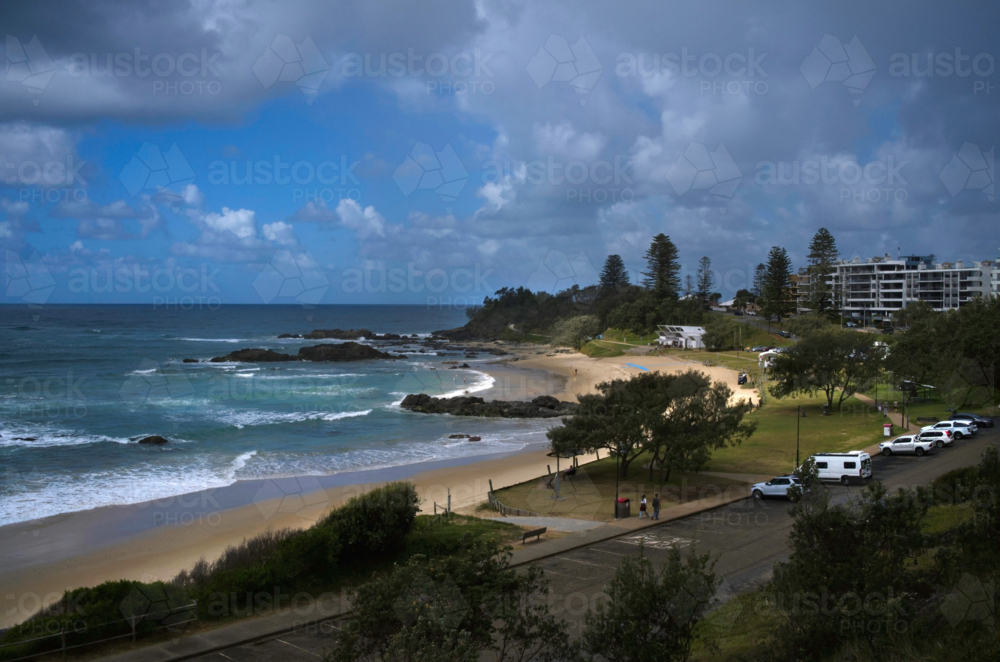 Beach with trees and buildings, sun and clouds - Australian Stock Image