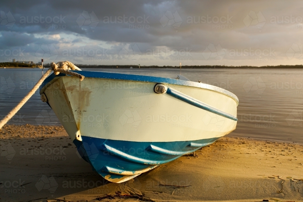 Beached boat sunlit with stormy sky - Australian Stock Image