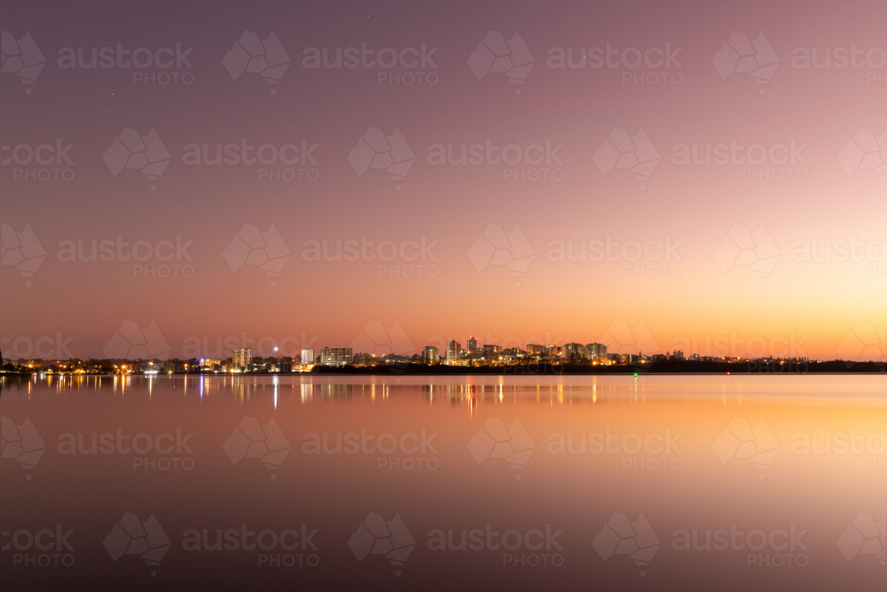 Beachside town in the distance lit up before dawn across inlet - Australian Stock Image