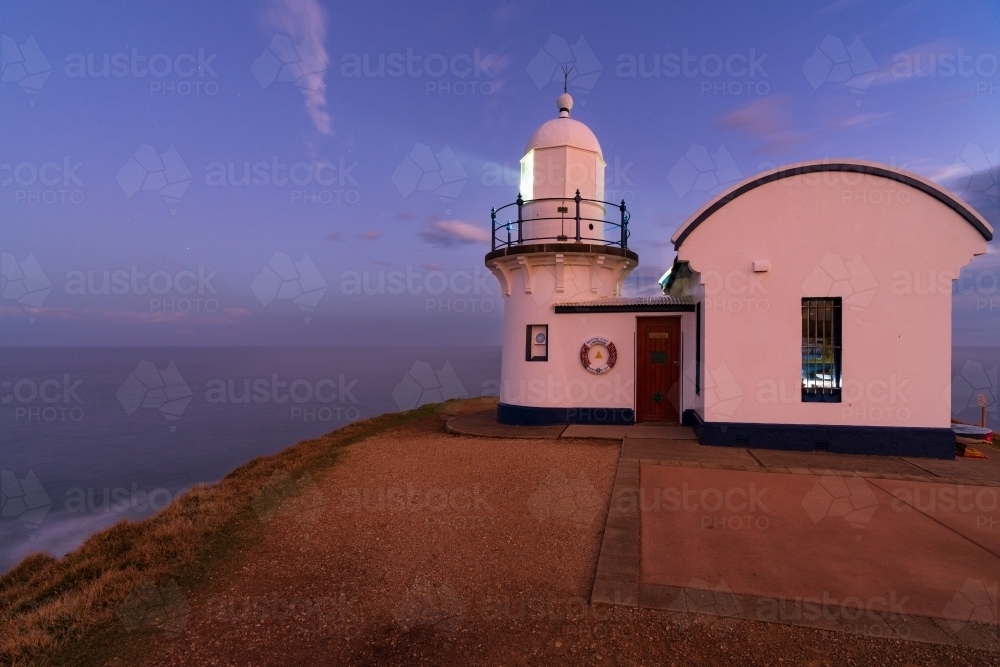 Beams of light coming from a short lighthouse on top of a hill at twilight - Australian Stock Image