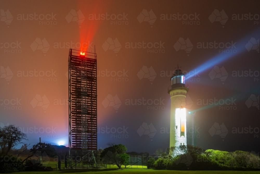 Beams of light from a lighthouse and beacon tower on a dark foggy night - Australian Stock Image