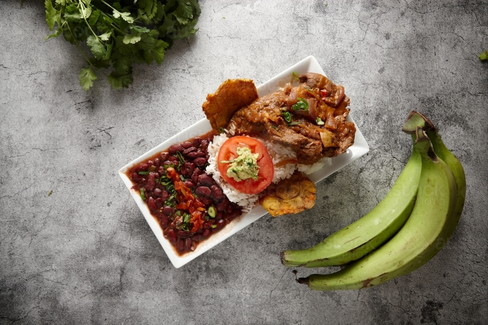 Beans rice and meat dish served in a rectangular plate on a concrete counter with green banana. - Australian Stock Image