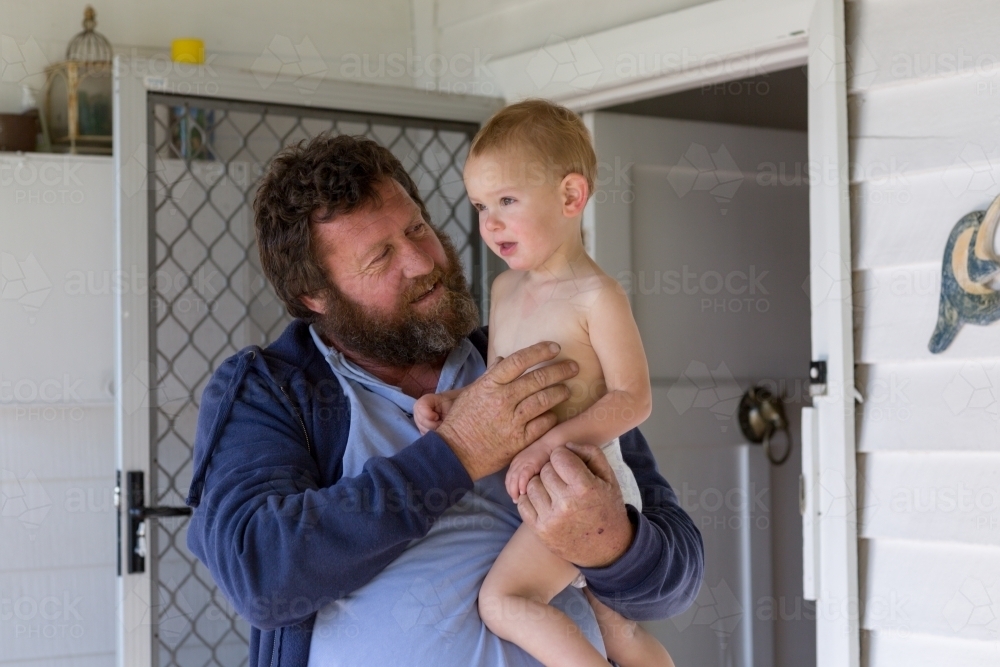 Bearded man holding child outside front door - Australian Stock Image