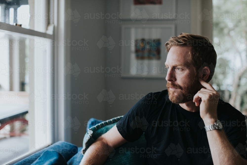 Bearded man seated looking out window - Australian Stock Image
