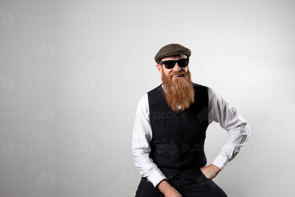 Bearded man sitting and smiling at camera wearing sunglasses - Australian Stock Image