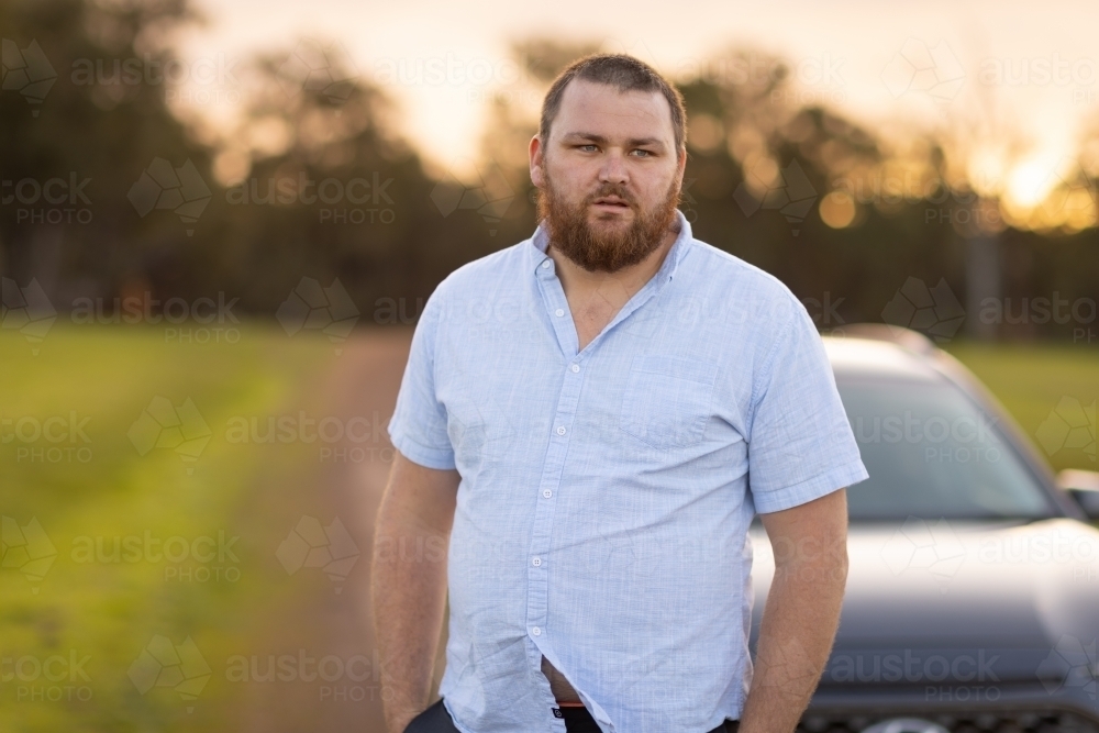 bearded man standing near car in the country - Australian Stock Image