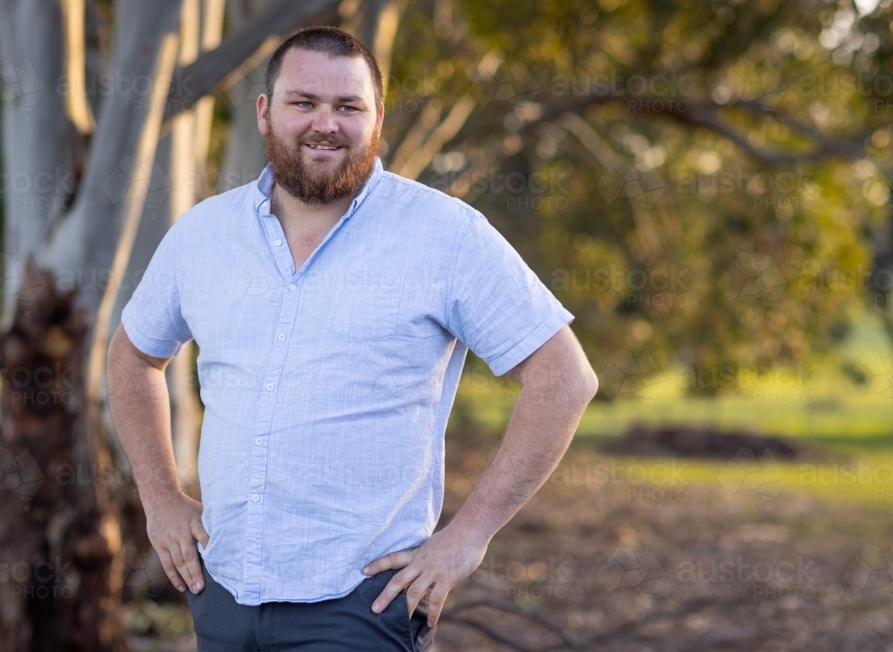 bearded man with hands on hips standing outdoors with trees in background - Australian Stock Image