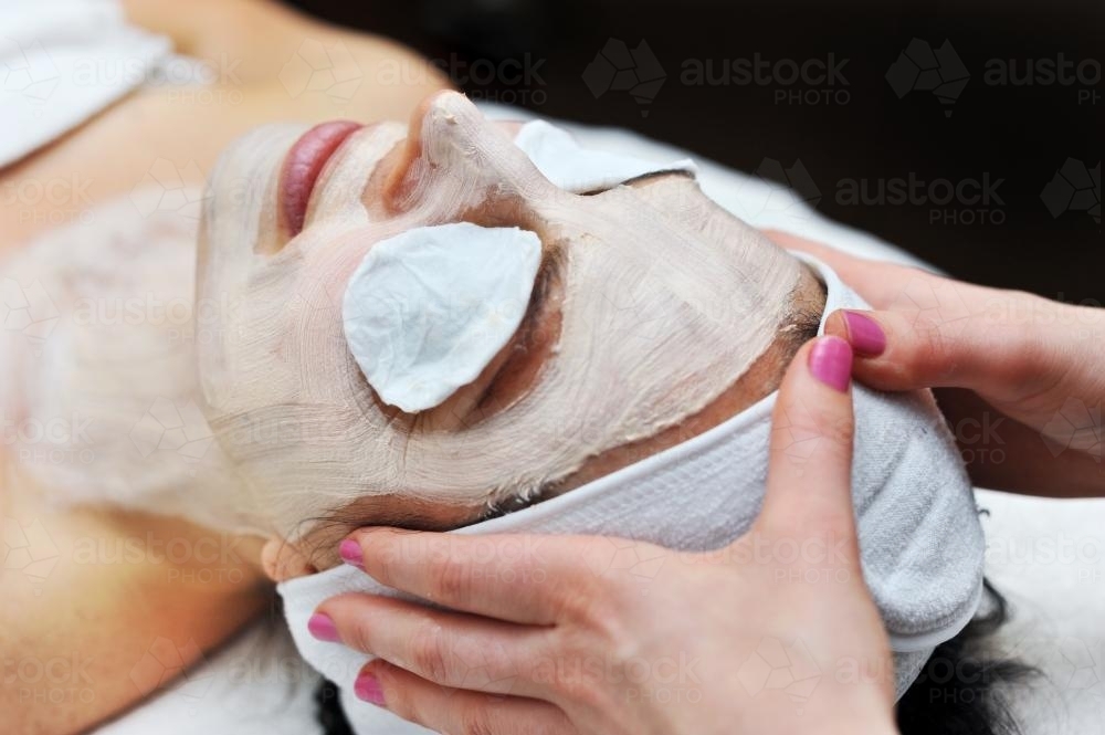 beautician hands on a client's head during a facial - Australian Stock Image