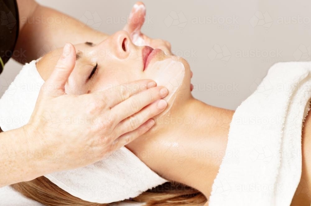 beautician hands on client's head during a facial - Australian Stock Image