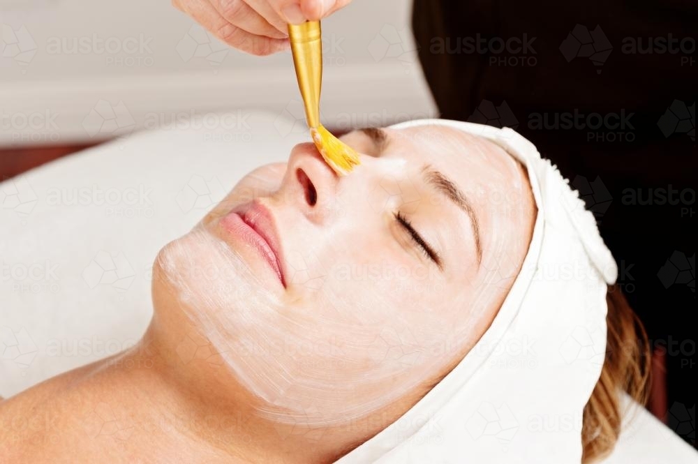 beautician uses a brush to apply cleanser during a facial - Australian Stock Image