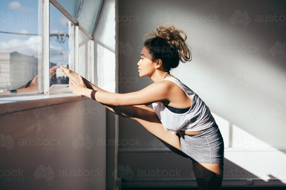 Beautiful 20s girl stretching her leg in a dance studio - Australian Stock Image