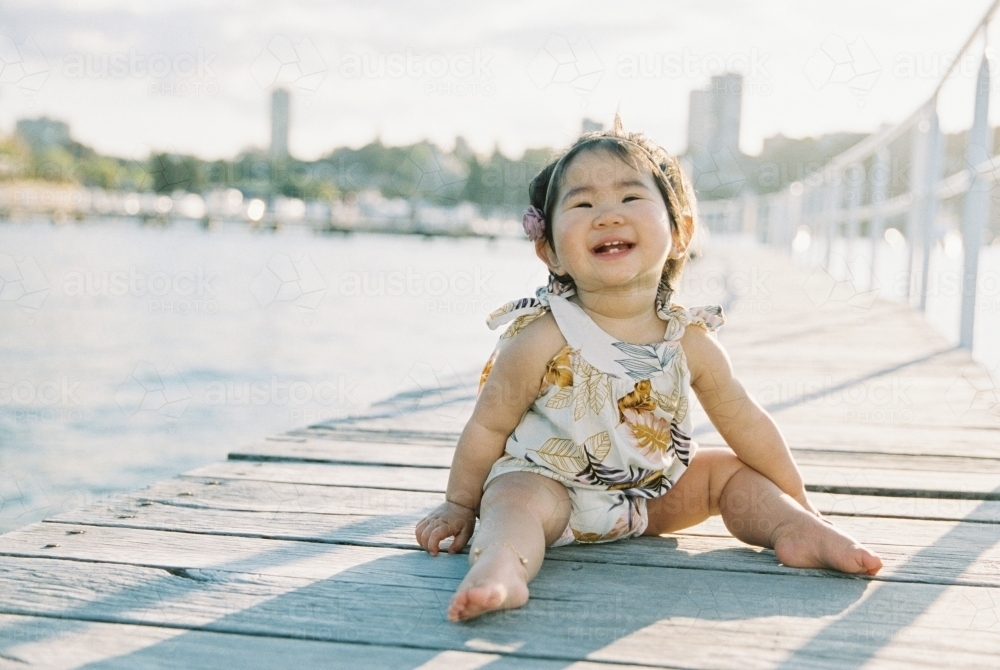 Beautiful Asian baby girl smiling and laughing on a wharf - Australian Stock Image