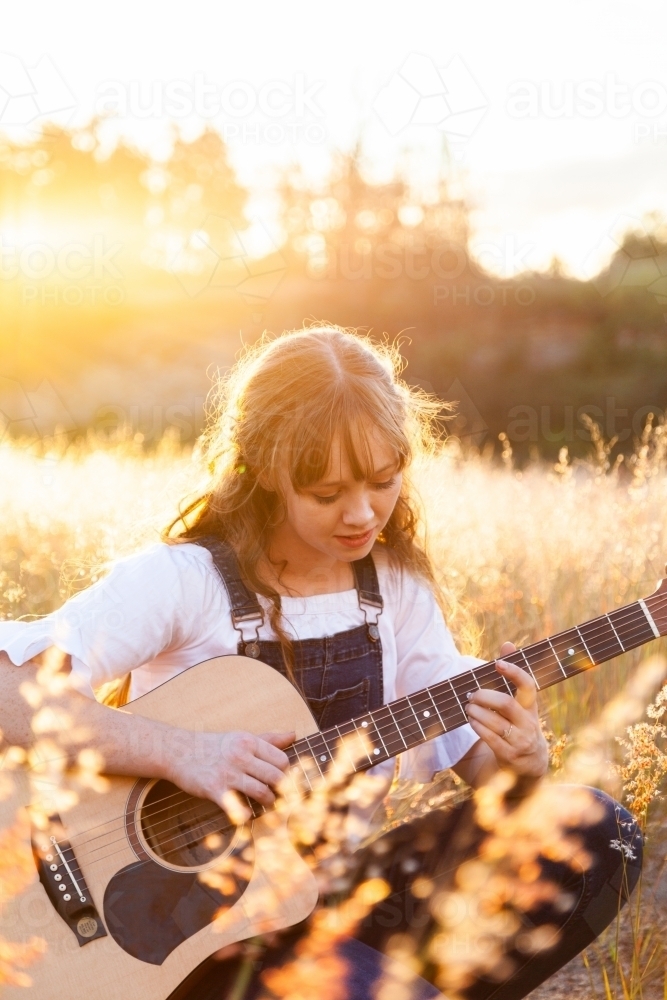 Beautiful scene of golden sunlight back lighting young female musician in grass - Australian Stock Image