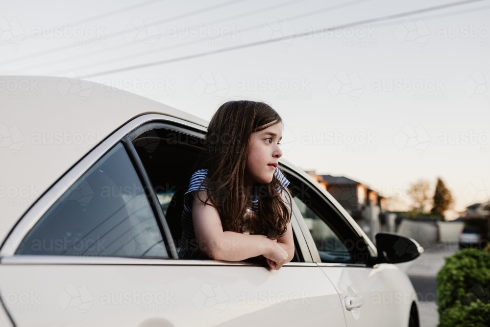 Smiling young girl leaning out the open window of the family car parked in the driveway - Australian Stock Image