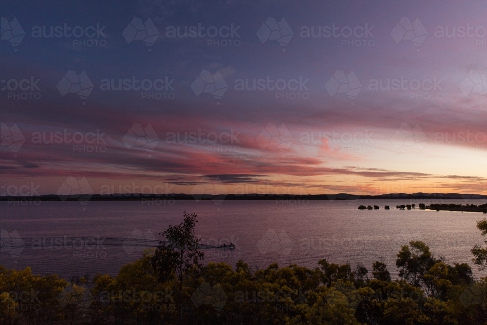 Beautiful sunset over large dam of water with wattle trees in foreground - Australian Stock Image