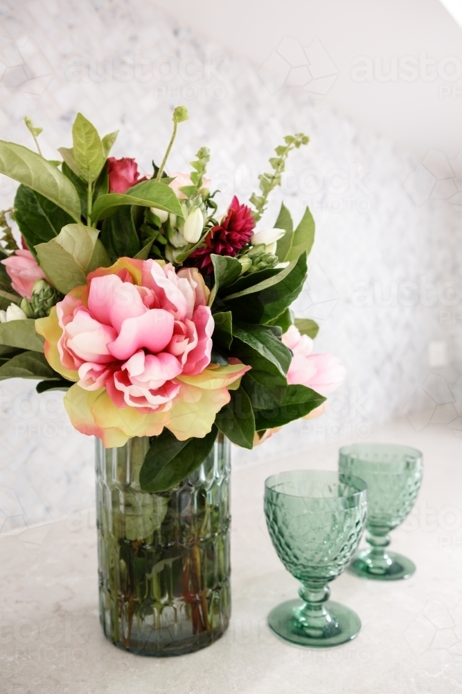 Beautiful vase of fresh cut flowers on a kitchen counter with vintage glasses - Australian Stock Image