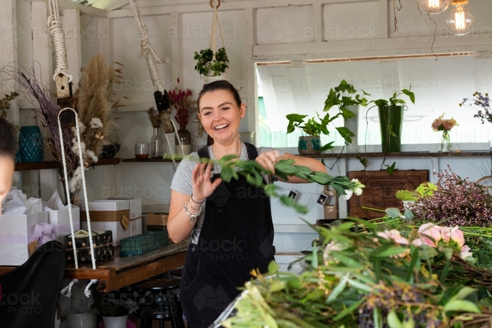Beautiful young florist laughing and enjoying her work preparing flowers for an event - Australian Stock Image