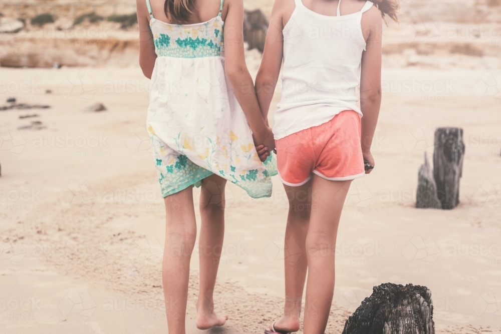 Behind view of two girls walking along the beach holding hands - Australian Stock Image