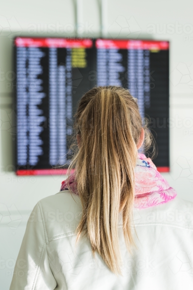 behind view of young woman reading the departures board at the airport - Australian Stock Image