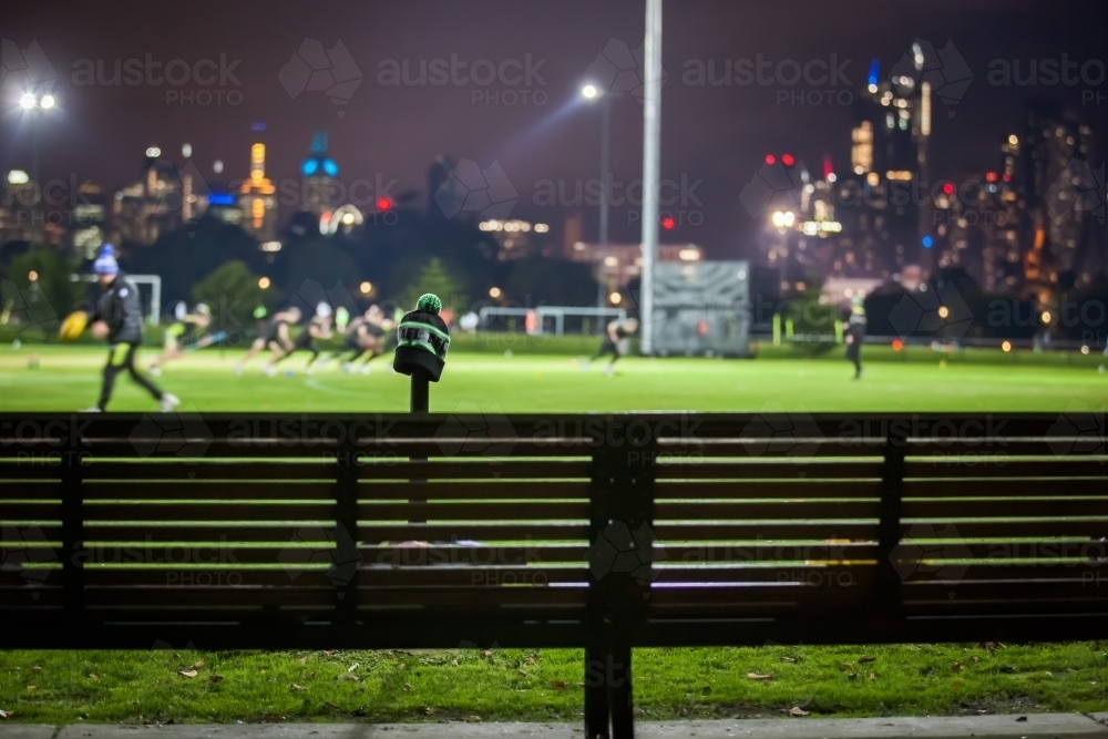 Bench seat at a sports ground with team training and city in background - Australian Stock Image