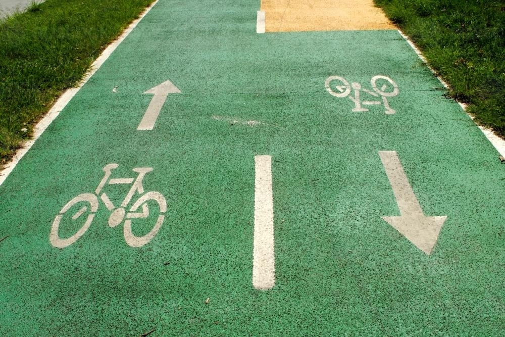 Bicycle and arrow signs painted in white on green asphalt - Australian Stock Image