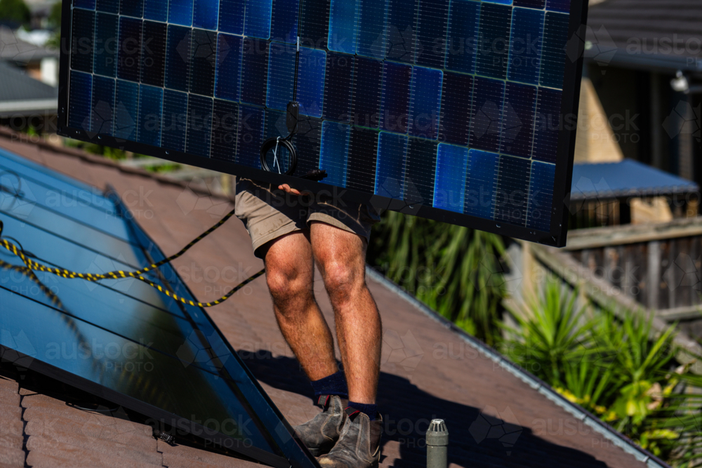 bifacial solar panels being carried on rooftop during solar system installation by electrician - Australian Stock Image