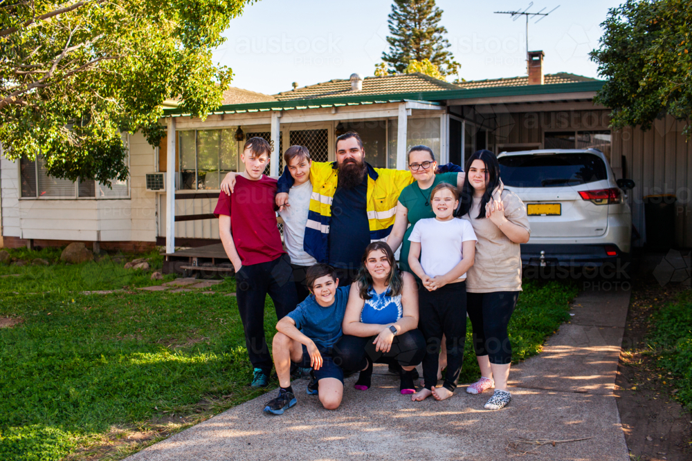 Big Aussie family with teenaged kids smiling together in front yard after dad came home after work - Australian Stock Image