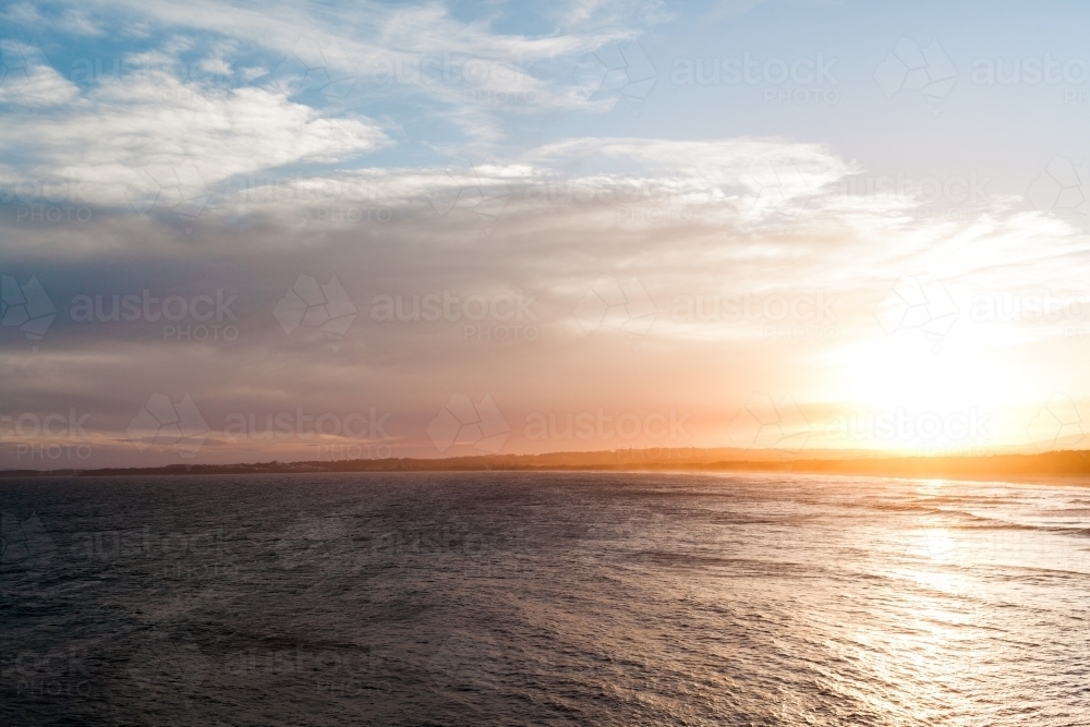 Big, blue, smooth ocean surrounds distant land on the horizon at sunset - Australian Stock Image