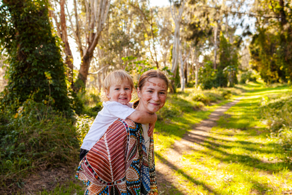 Big sister giving little brother a piggyback ride in nature - Australian Stock Image