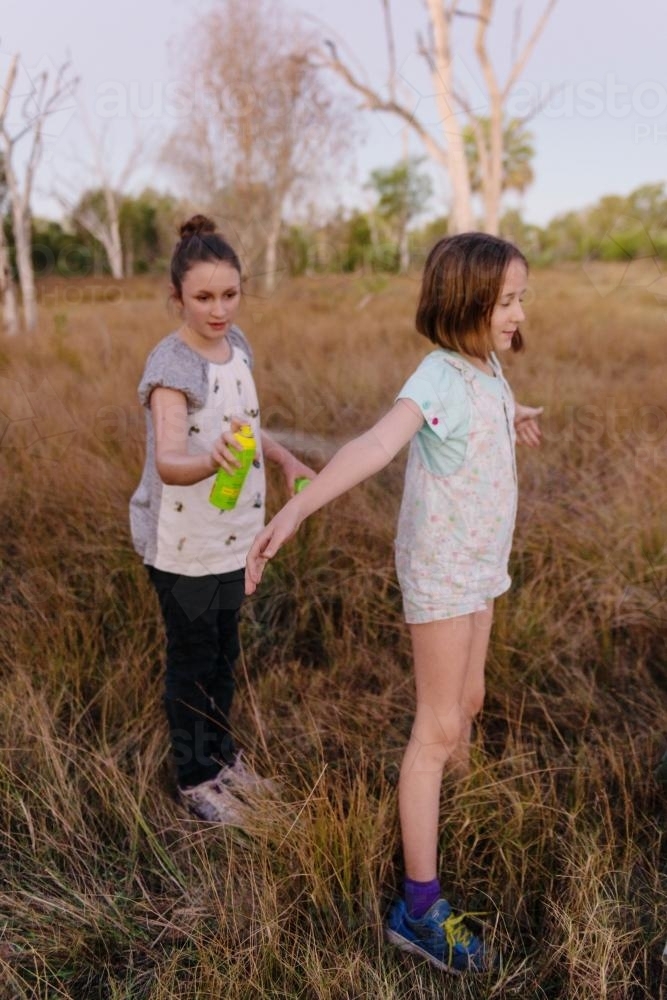 big sister sprays little sister with insect repellant - Australian Stock Image