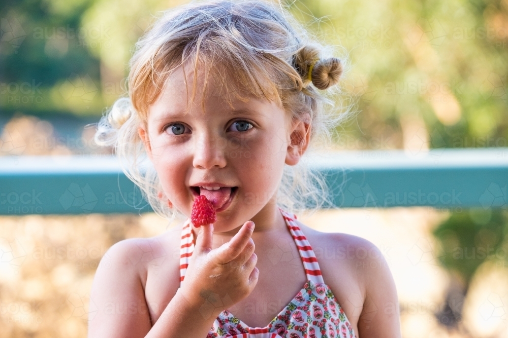 Big wide eyed little girl with a big fresh raspberry - Australian Stock Image