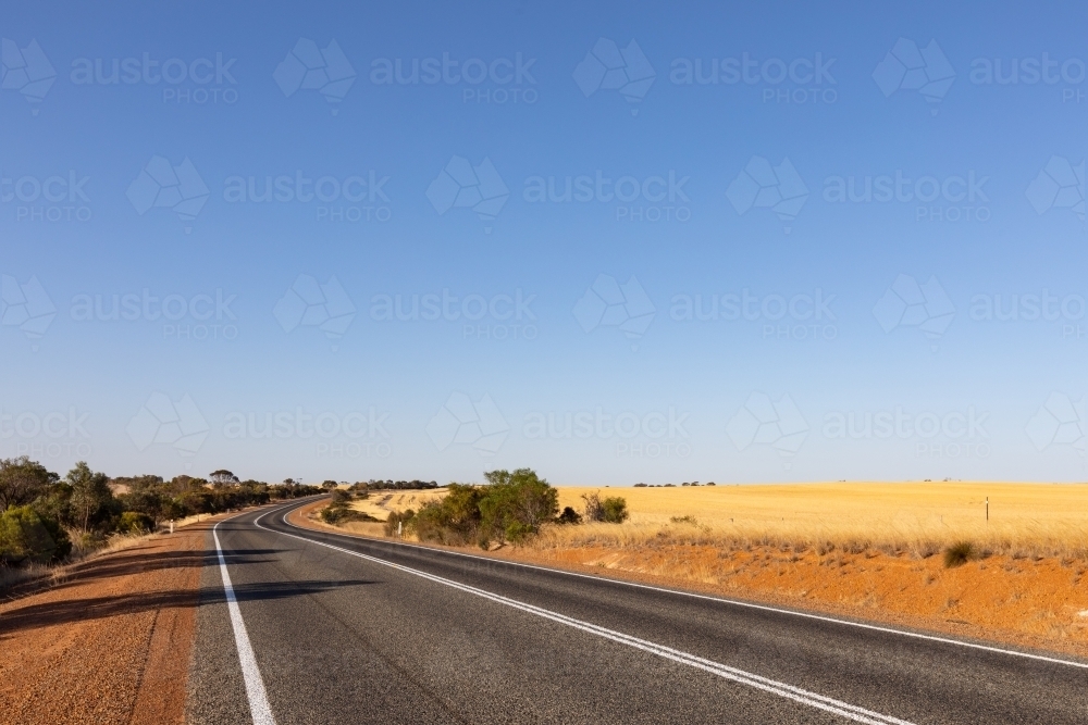 Bitumen road through dry landscape with blue sky - Australian Stock Image