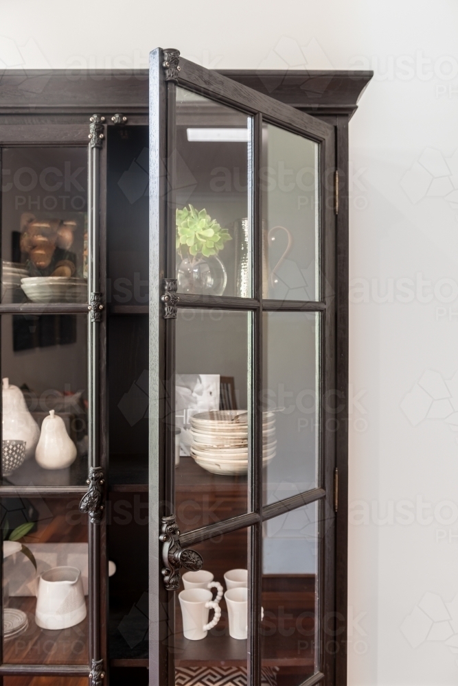 black french inspired tall cabinet with glass doors, filled with books and pottery - Australian Stock Image