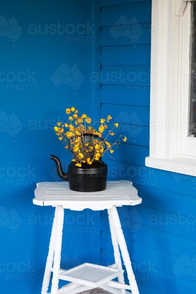 Black kettle with yellow flowers, on a white stand - Australian Stock Image