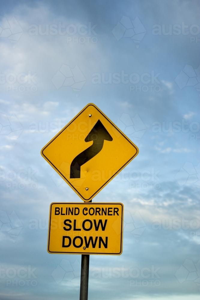 Blind corner slow down road sign against clouds - Australian Stock Image