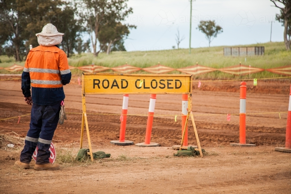 Bloke in hi-vis clothing standing beside road closed sign - Australian Stock Image