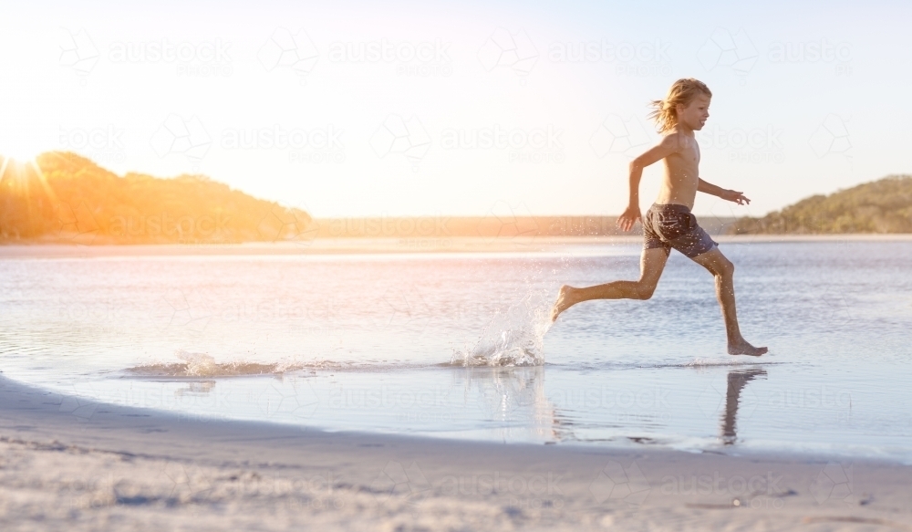 Blond-haired boy running through water on the beach - Australian Stock Image