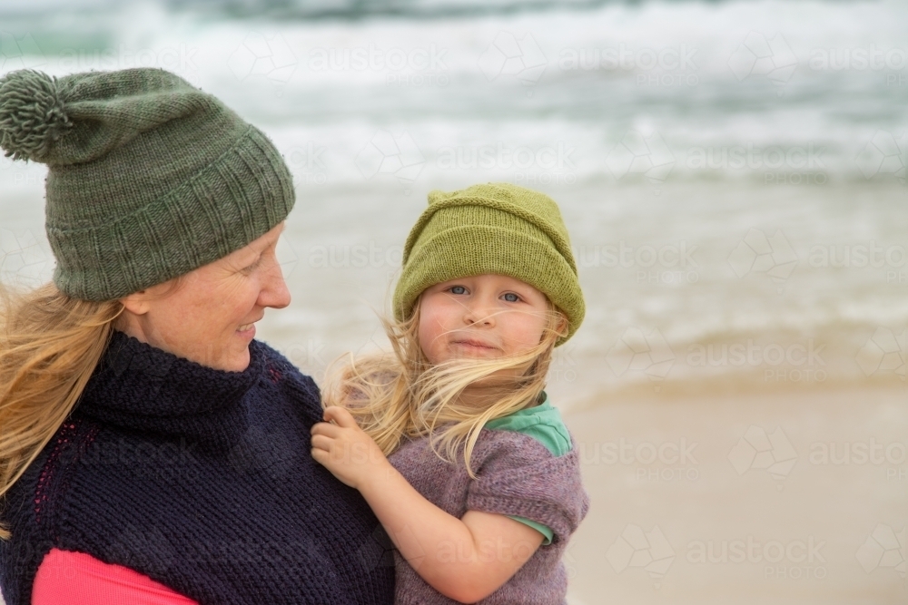 Blonde mother carrying toddler daughter at the beach on a stormy day. - Australian Stock Image