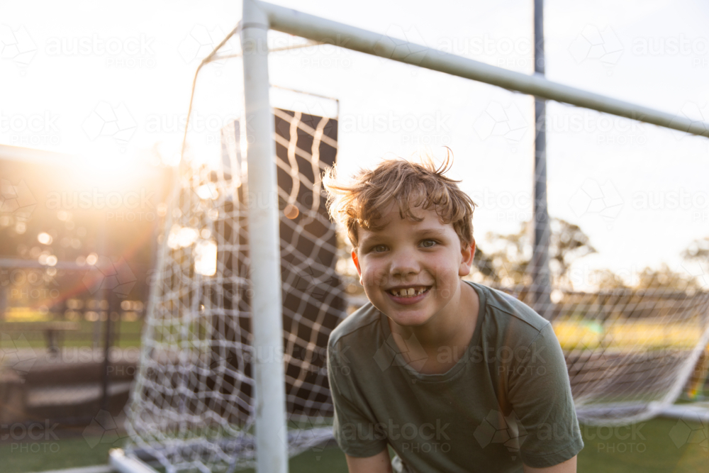 blonde boy smiling and leaning forward in front of a soccer goal - Australian Stock Image